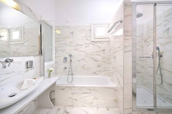 Ein elegantes Badezimmer im Kamari Hotel mit Marmorwänden, einer Badewanne und einer separaten Dusche.