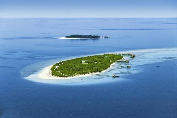 Luftaufnahme des Reethi Beach Resorts, einer Insel mit grüner Vegetation und weißen Stränden, umgeben von blauem Ozean.