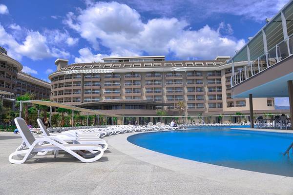 Außenbereich eines Hotels mit Pool und weißen Sonnenliegen unter Palmen.