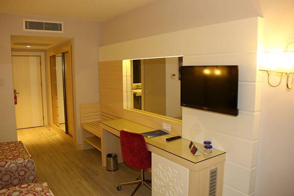 Hotelzimmer mit Schreibtisch, Fernseher, rotem Stuhl und Lampe an der Wand.