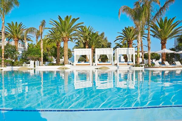 Pool des Grecotel Caramel Boutique Resorts mit weißen Sonnenschirmen und Loungestühlen