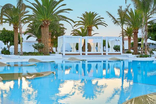 Außenpool des Grecotel Caramel Boutique Resort mit weißen Sonnenliegen und weißen Pavillons.
