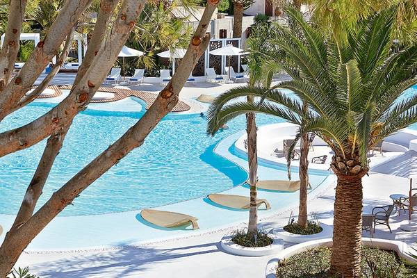 Außenbereich des Grecotel Caramel Boutique Resort mit Swimmingpool, Loungemöbeln und Palmen.