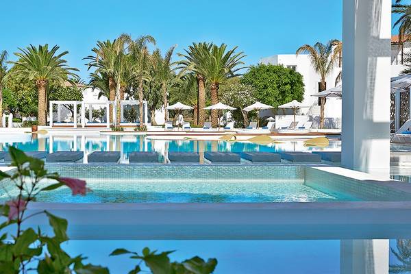 Außenpool des Grecotel Caramel Boutique Resort mit weißen Säulen und Loungemöbeln.
