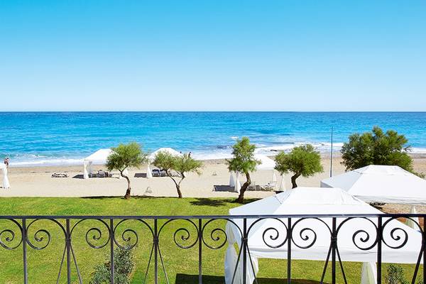 Aussicht auf den Strand vom Grecotel Caramel Boutique Resort mit weißen Sonnenschirmen und grünem Rasen.