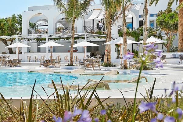 Außenbereich des Grecotel Caramel Boutique Resorts mit Pool, Sonnenliegen und Schirmen.