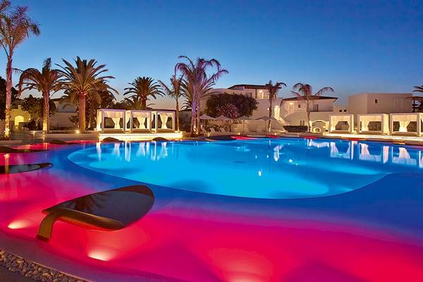 Der Pool des Grecotel Caramel Boutique Resort bei Nacht mit farbigen Lichtern.