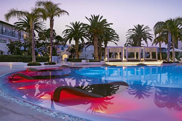 Außenbereich des Grecotel Caramel Boutique Resort mit Swimmingpool, Loungeliegen und Palmen