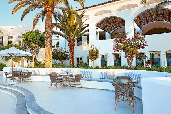 Außenbereich des Grecotel Caramel Boutique Resort mit weißer Architektur, Palmen und gemütlichen Sitzgelegenheiten