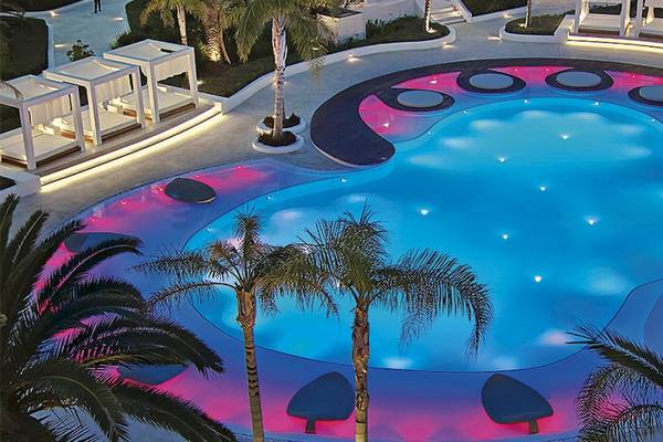 Pool des Grecotel Caramel Boutique Resorts mit blauen und pinken Lichtern bei Nacht