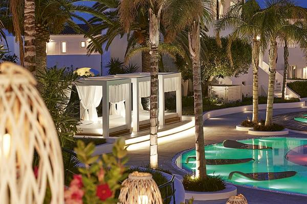 Nachtansicht des Grecotel Caramel Boutique Resorts mit beleuchteten Liegebetten und Swimmingpool.