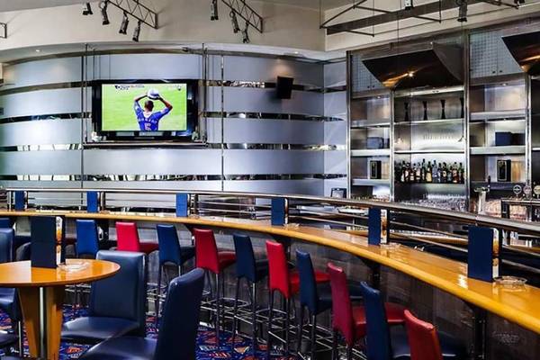 Innenansicht der Bar im Hilton Dubai Jumeirah Resort mit Fernseher und blauen, roten und gelben Stühlen.