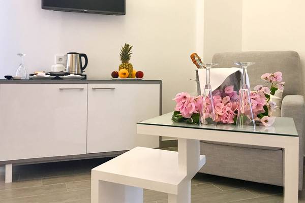 Wohnbereich im Bruskos Hotel mit Fernseher, Tisch mit Blumen und Früchten, und Sofa.