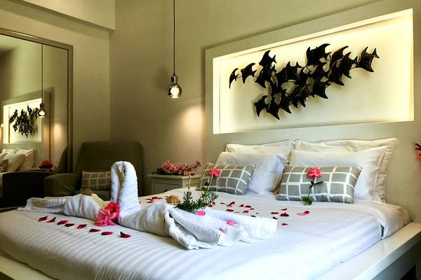Schlafzimmer im Bruskos Hotel & Suites mit einem Bett, weißen Laken, Kissen, Blumen und weißen Strähnen.