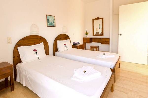Innenansicht eines Doppelzimmers im Bruskos Hotel & Suites mit zwei Betten, weißem Bettzeug und Holzmöbeln.