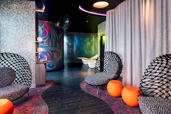 Loungebereich im W Dubai - The Palm mit bunten Wandmalereien, modernen Möbeln und orangefarbenen Hockern.