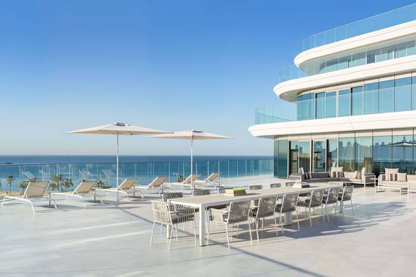 Außenterrasse des W Dubai - The Palm mit Blick auf das Meer, Lounge-Sesseln und Sonnenschirmen.