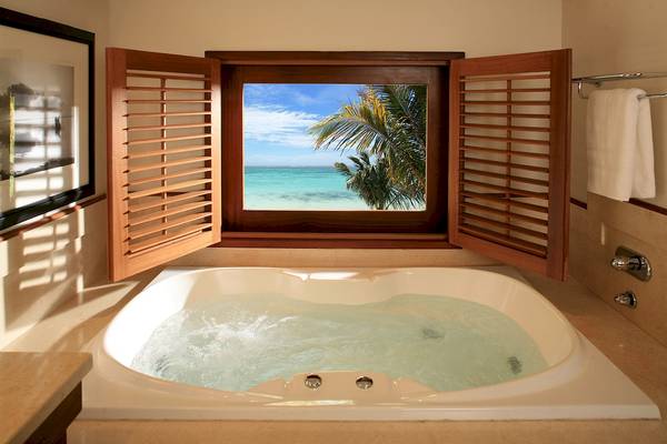Ein Badezimmer mit einem Whirlpool und Meerblick durch ein Fenster mit Holzjalousien.