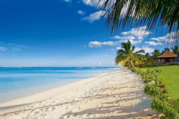 Strand des LUX Le Morne Hotels mit weißen Sand, blauem Meer, Palmen und traditionellem Haus