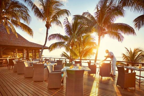 Außenterrasse des LUX Le Morne Hotels bei Sonnenuntergang mit geselligem Ambiente und Blick aufs Meer.
