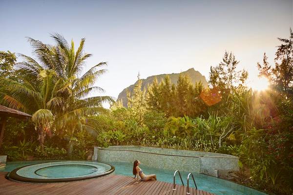 Eine Frau sitzt am Poolrand im LUX Le Morne Hotel, umgeben von tropischer Vegetation und Blick auf den Berg.