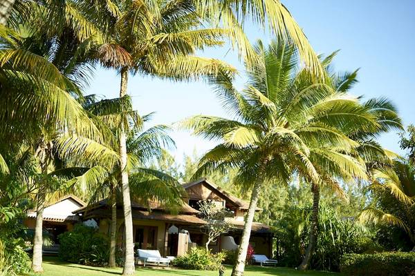 Außenansicht des LUX Le Morne Hotels, umgeben von Palmen und Rasen, mit weißen Liegestühlen.