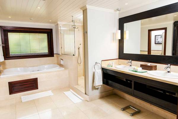 Badezimmer im LUX Le Morne Hotel mit Badewanne, Dusche, Waschbecken und Spiegel.