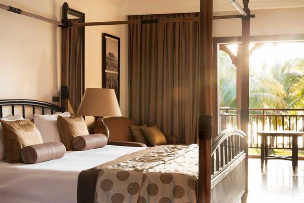 Schlafzimmer im LUX Le Morne Hotel mit Himmelbett, Kissen, Lampen und Balkon.