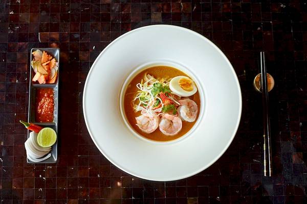 Thai Curry mit Garnelen und Ei, serviert in einem weißen Teller mit Beilagen auf einem Tisch.