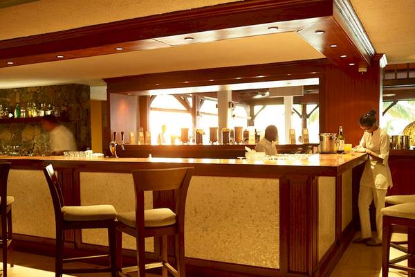 Die Bar im LUX Le Morne Hotel mit Barkeepern, die Getränke zubereiten und eine Person, die an der Theke steht.