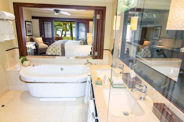 Badezimmer im LUX Le Morne Hotel mit Badewanne, Spiegel und Blick auf das Schlafzimmer.