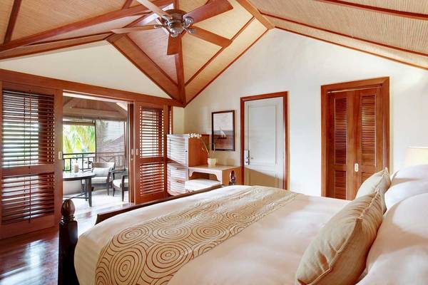 Innenansicht des Schlafzimmers im LUX Le Morne Hotel mit einem großen Bett, Holzdecken und Fenstern.