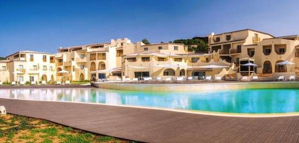Das Cala Cuncheddi Hotel mit großem Pool und Liegestühlen vor einem Gebäude.