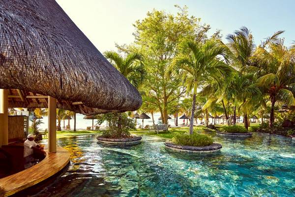 Außenbereich des Pools mit Bar im LUX Le Morne Hotel, umgeben von Palmen und Meer.