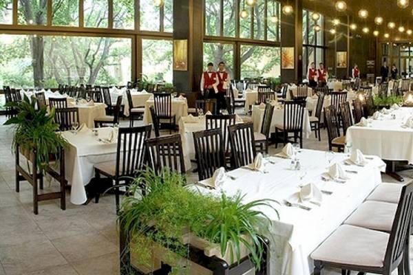 Hotelfoyer mit gedeckten Tischen und Sesseln, zwei Angestellte in roten Westen stehen im Hintergrund.