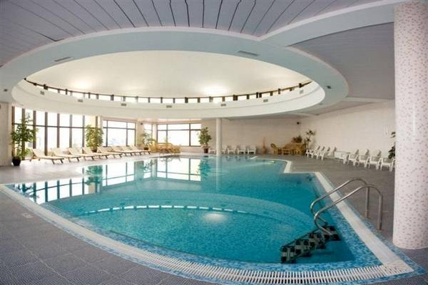 Innenansicht eines Schwimmbads im Riviera Beach Hotel mit geometrischem Design und umliegenden Liegestühlen.