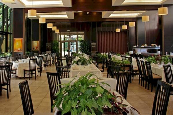 Ein großer Speisesaal im Riviera Beach Hotel mit vielen gedeckten Tischen, Pflanzen und Kunstwerken an den Wänden.