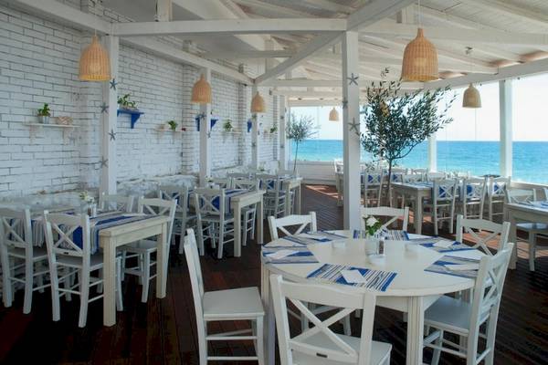 Hotel Terrasse mit Blick auf das Meer und weißen Tischen und Stühlen.