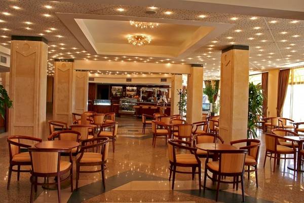 Foyer des Riviera Beach Hotels mit Tischen und Stühlen, beleuchtete Decke und Bar.