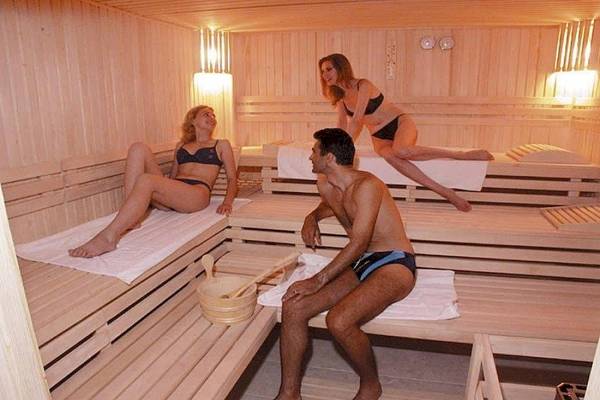 Drei Personen, zwei Frauen und ein Mann, entspannen sich in einer Holzsauna des Riviera Beach Hotels.