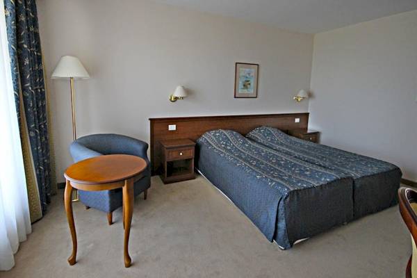 Ein Doppelbettzimmer im Riviera Beach Hotel mit einem Doppelbett, einem Nachttisch, einem Stuhl und einer Stehlampe.