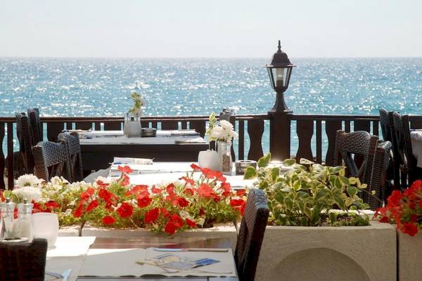 Terrasse mit Meerblick im Riviera Beach Hotel mit blumengeschmückten Tischen und einem Blick auf das offene Meer.