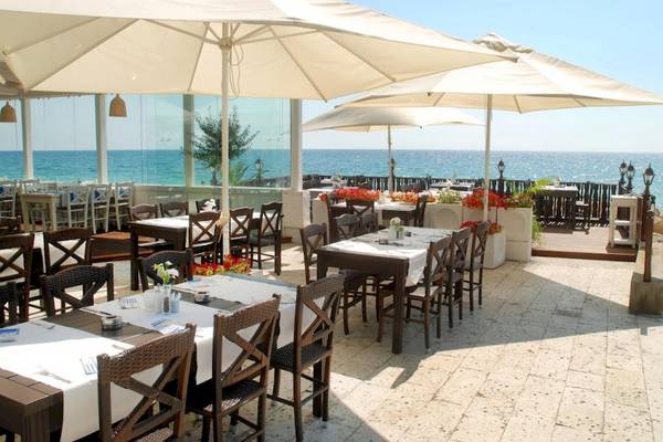 Terrasse des Riviera Beach Hotels mit Blick auf das Meer und gedeckten Tischen unter Sonnenschirmen.