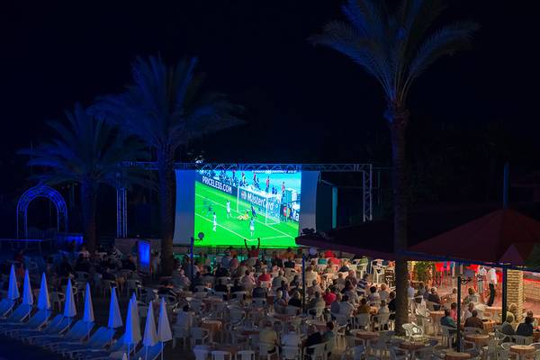 Foto von einer Abendveranstaltung im Miramare Queen Hotel, bei der ein Fußballspiel auf einer großen Leinwand gezeigt wird.