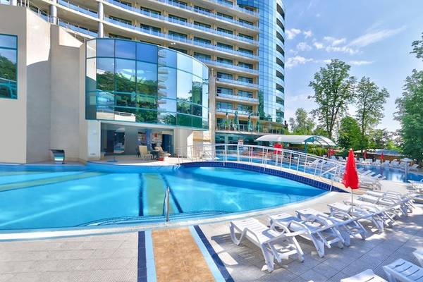 Außenpool des Marina Grand Beach Hotels mit weißen Liegestühlen und roten Sonnenschirmen.