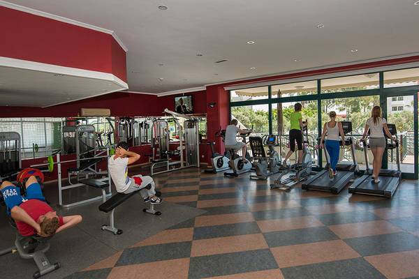 Fitnessstudio im Miramare Queen Hotel mit verschiedenen Trainingsgeräten und Personen, die trainieren.