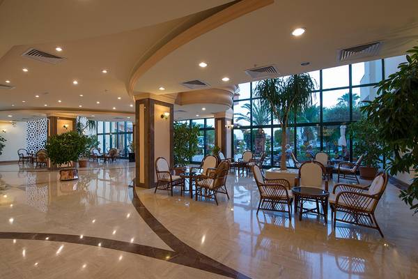 Lobby des Miramare Queen Hotels mit Möbeln, Pflanzen und großen Fenstern.