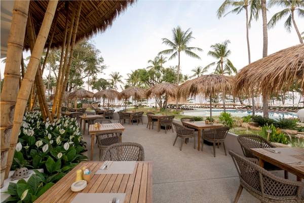 Terrasse des Eden Beach Khao Lak Resorts mit Tischen, Stühlen und Sonnenschirmen.