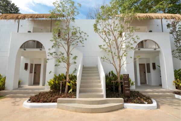Vorderansicht des Eden Beach Khao Lak Resorts und Spas mit weißen Wänden, Treppen und Bäumen.