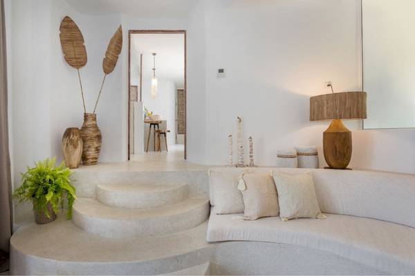Inneneinrichtung des Eden Beach Khao Lak Resort & Spa mit weißen Wänden, einer Couch, Kissen und einer Lampe.